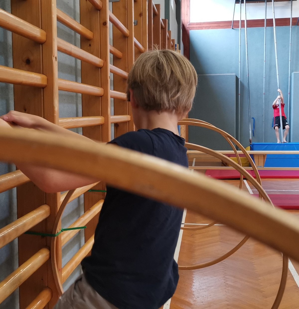 Kind klettert auf Sprossenwand und durch darauf befestigte Hula Hoop-Reifen